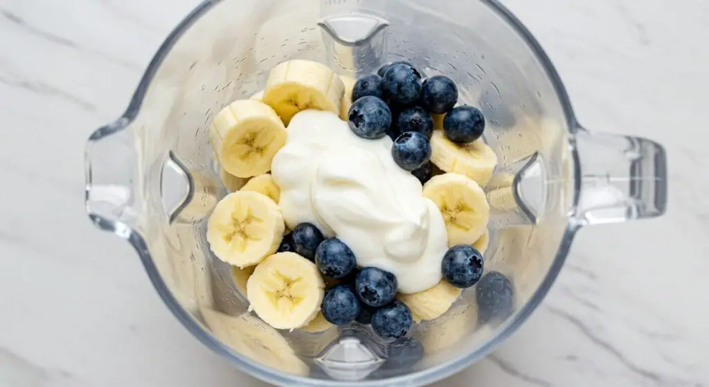 Close-up of the creamy, lavender-hued Banana-Blueberry Smoothie being poured from a blender into a clear glass, showcasing its smooth texture.