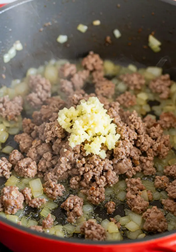 Dry orzo pasta, browned crumbled sausage, chopped onion, and corn kernels in a Dutch oven with chicken broth just added, before simmering, for the One-Pot Orzo with Sausage recipe