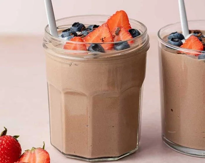 Bowl of rich chocolate protein pudding topped with chocolate shavings and berries