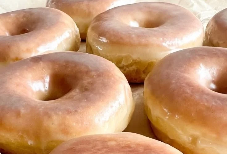 Freshly made glazed sourdough donuts on a display tray