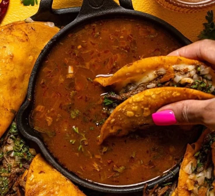 Delicious Birria Tacos with tender meat and rich sauce served with lime and onions.