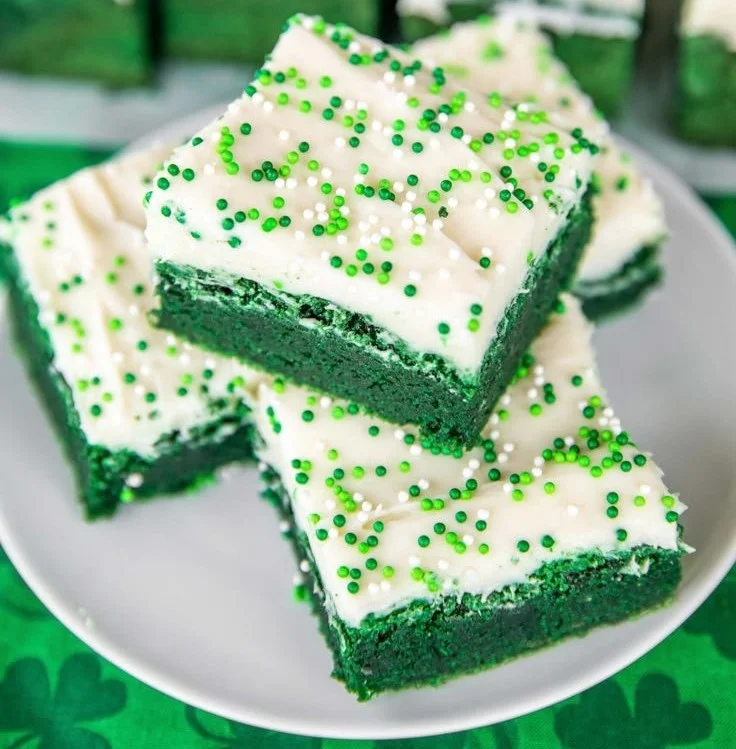 Delicious green velvet brownies with cream cheese frosting on a dessert plate.
