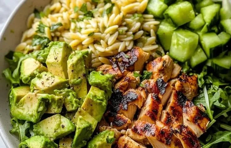 A colorful bowl of Grilled Chicken Orzo Salad with fresh vegetables and herbs.