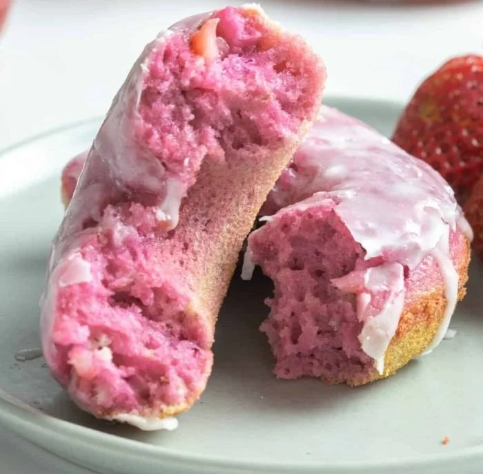 Freshly baked strawberry cake donuts topped with frosting and fresh strawberries