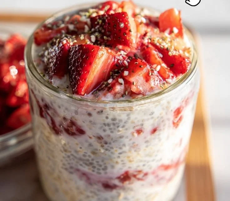 Fresh strawberry overnight oats in a glass topped with sliced strawberries.