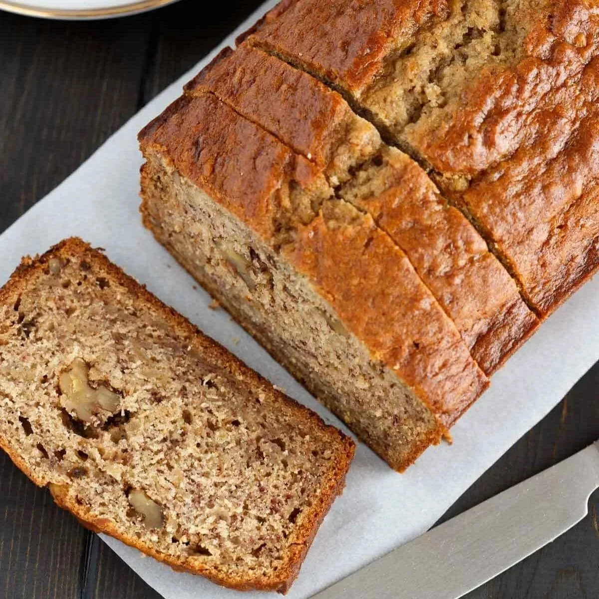 Sliced banana bread on a wooden cutting board with bananas in the background.
