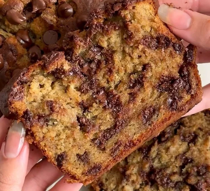 Slices of chocolate chip banana bread on a wooden table with chocolate chips scattered.
