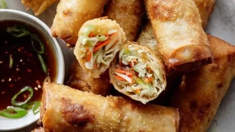 Golden crispy spring rolls served on a plate with dipping sauce.