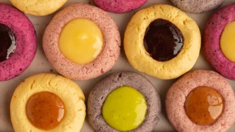 Colorful fruity thumbprint cookies topped with jam on a baking tray.