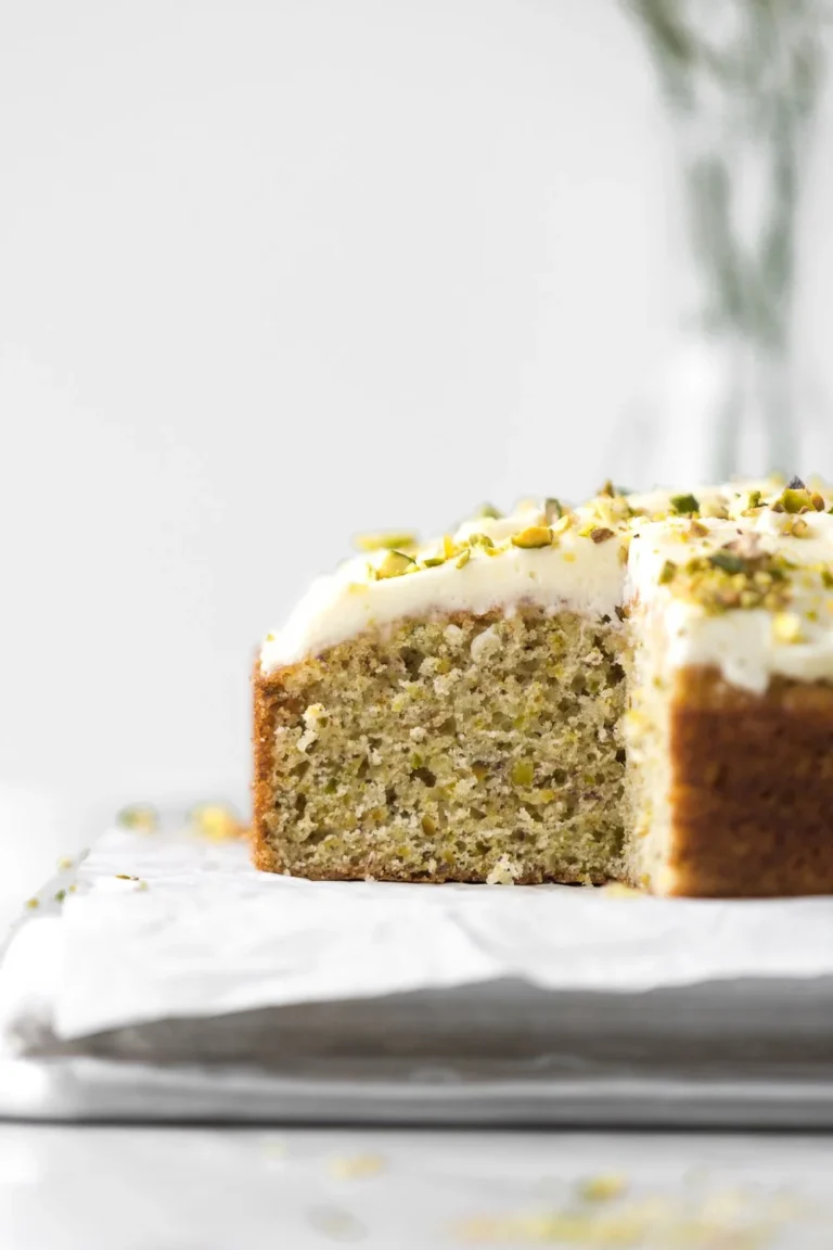 Lemon pistachio cake topped with smooth mascarpone frosting on a decorative plate.