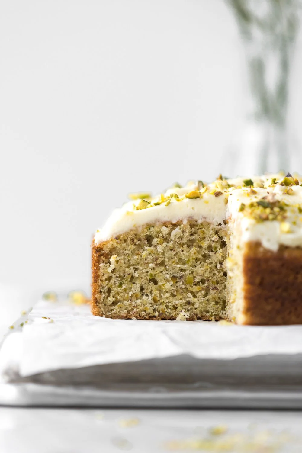 Lemon pistachio cake topped with smooth mascarpone frosting on a decorative plate.