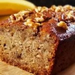 Slice of ultimate banana nut bread with nuts and ripe bananas