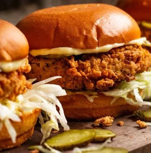 Ultra crunchy fried chicken burger with toppings on a wooden table.