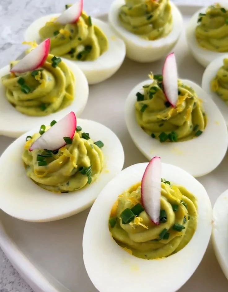 Plate of avocado deviled eggs garnished with herbs
