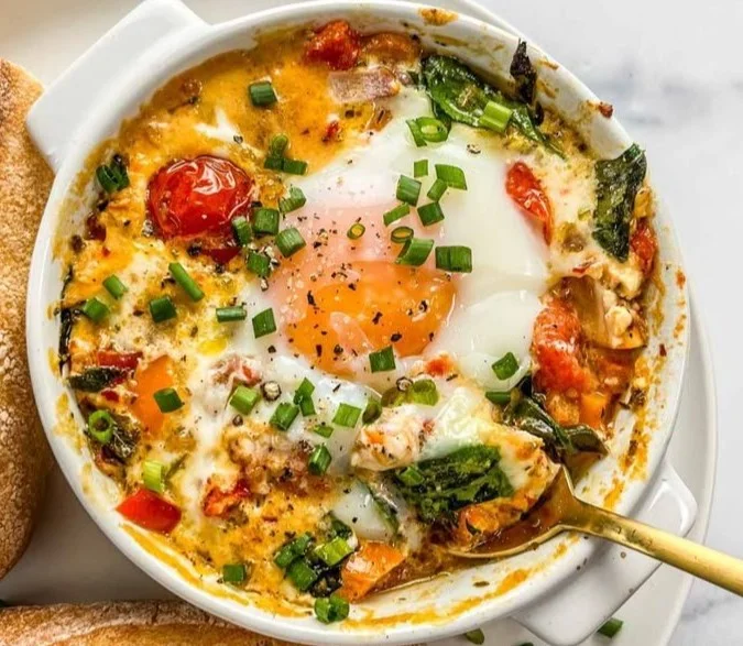 Delicious baked feta eggs with fresh tomatoes and spinach served in a baking dish