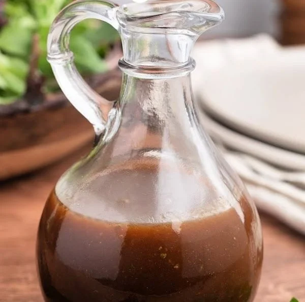 Homemade balsamic vinaigrette dressing in a glass jar with fresh herbs.