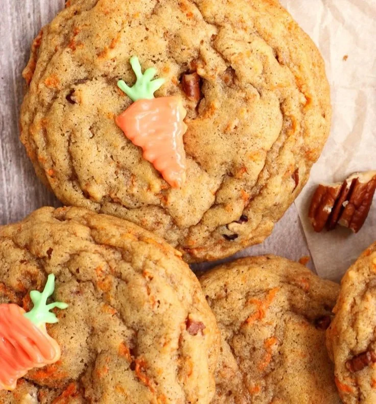 Chewy brown butter carrot cake cookies on a plate, garnished with nuts and frosting.