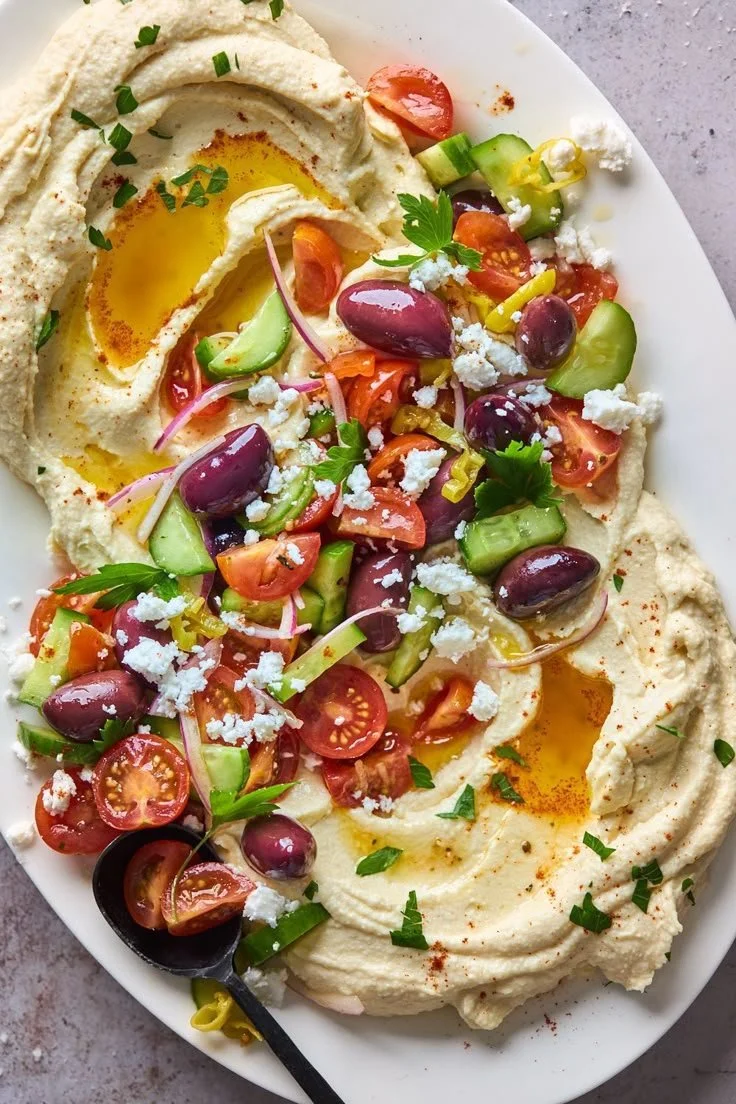 A bowl of Greek Style Loaded Hummus topped with olives and herbs.