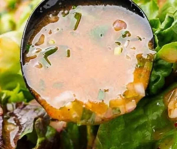 Bottle of homemade French vinaigrette with fresh herbs and salad ingredients.