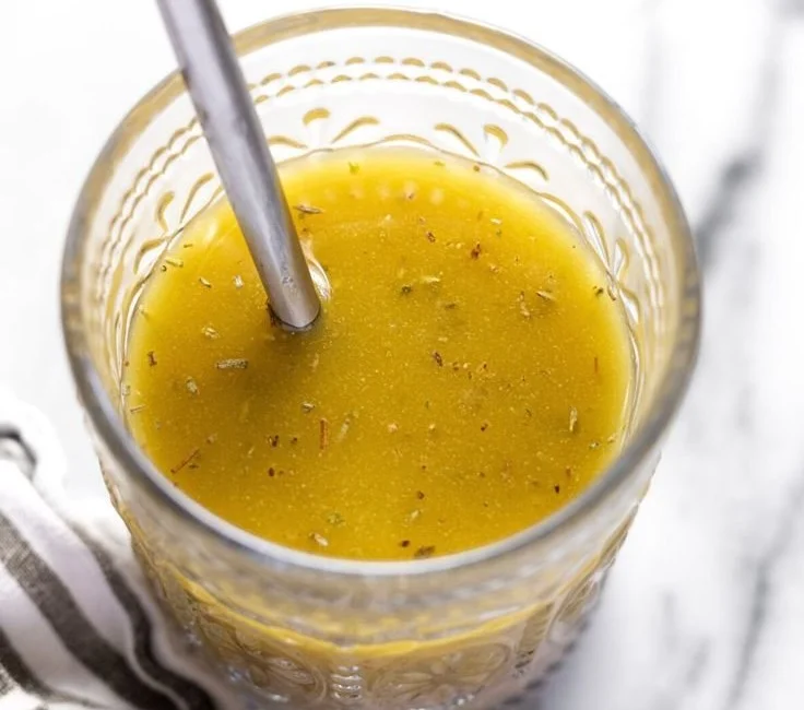 Homemade red wine vinaigrette in a glass jar with fresh herbs and spices.