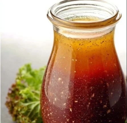 A bottle of red wine vinaigrette with fresh ingredients for salads.