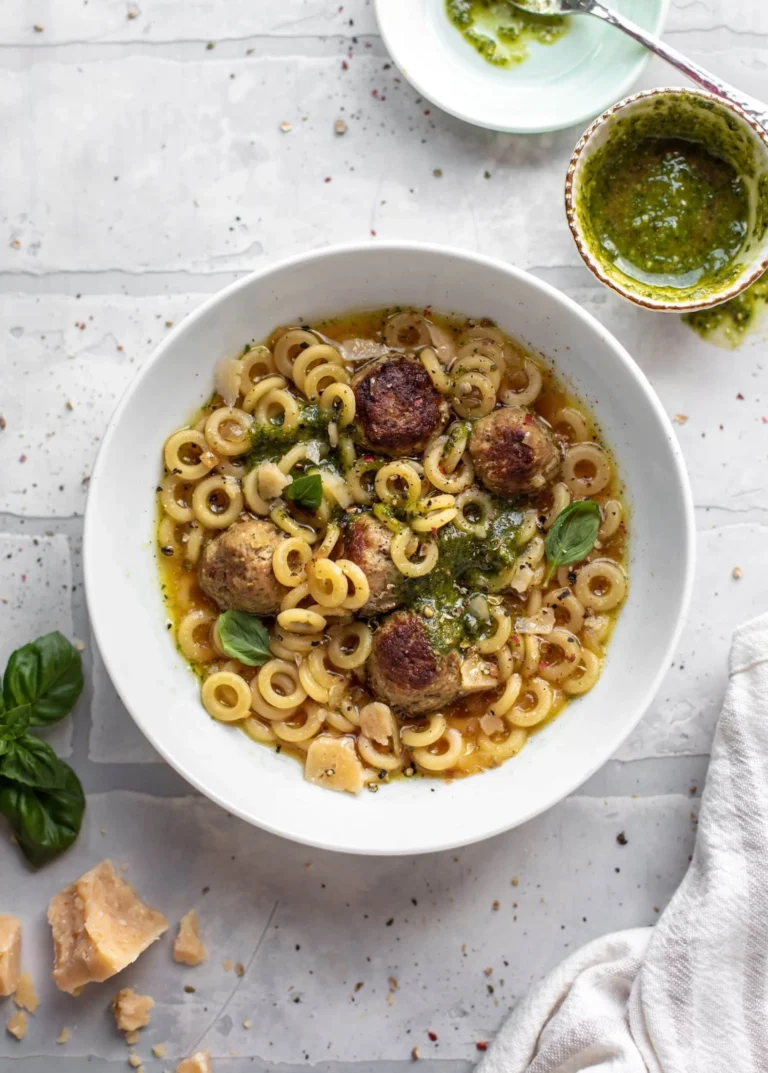 Bowl of Ultimate Summer Pesto Mini Meatball Soup garnished with fresh basil