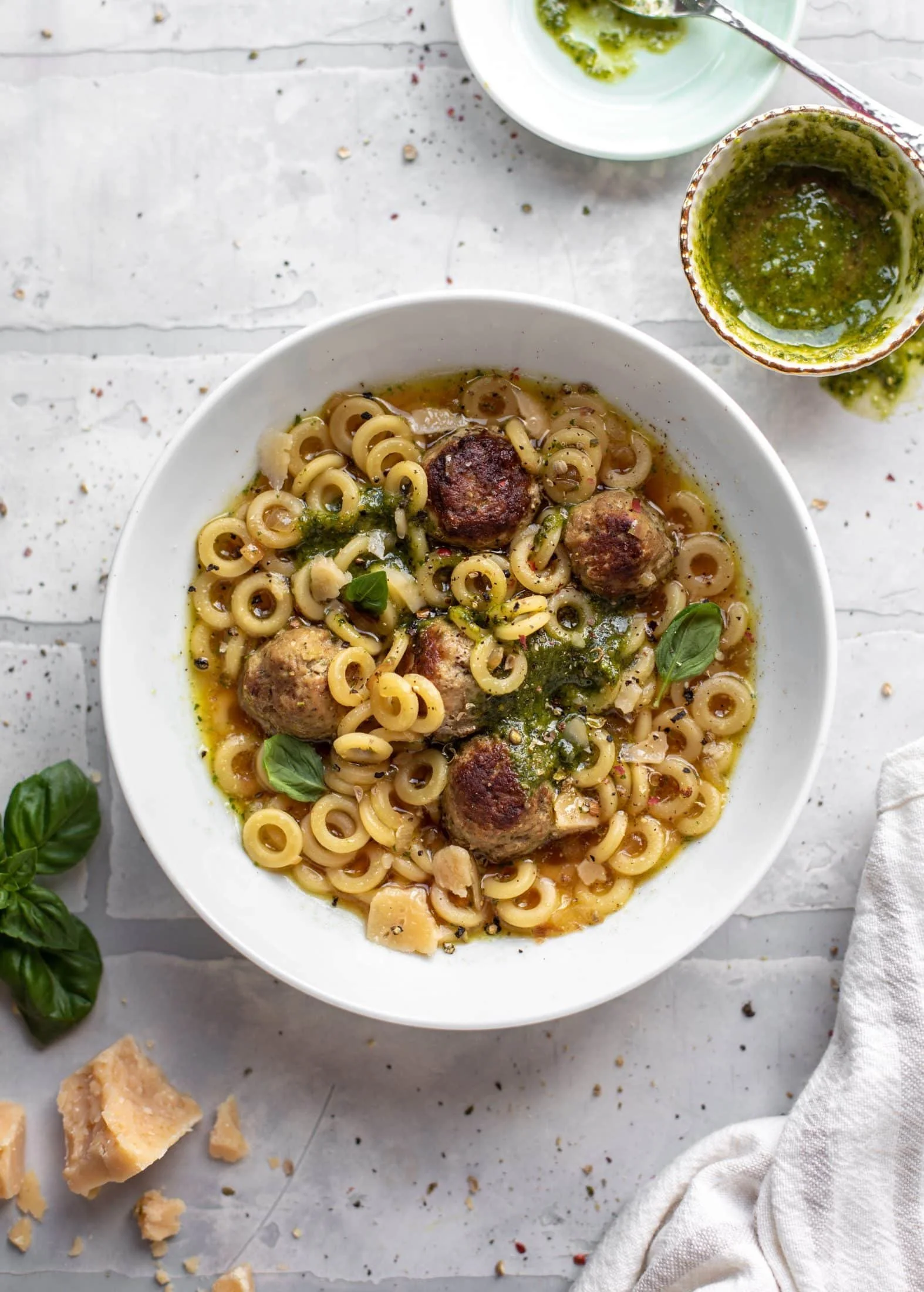Bowl of Ultimate Summer Pesto Mini Meatball Soup garnished with fresh basil