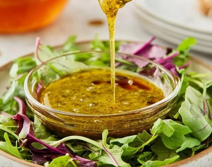 Homemade vinaigrette dressing in a glass jar with fresh herbs and ingredients.