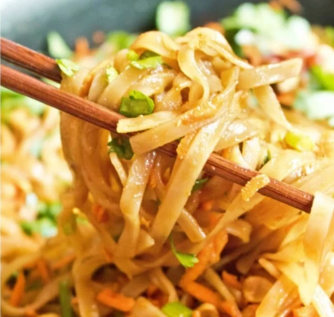 Bowl of sweet and spicy noodles garnished with vegetables and herbs