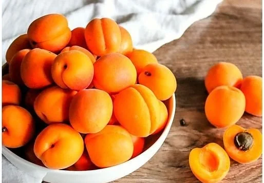 Jar of homemade apricot jam with fresh apricots in the background