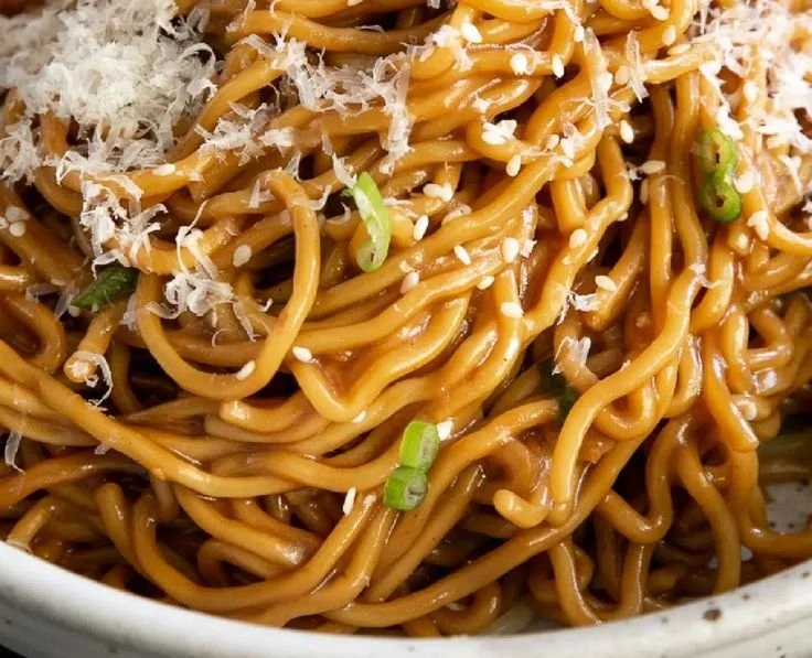 Plate of Asian garlic noodles garnished with herbs and vegetables