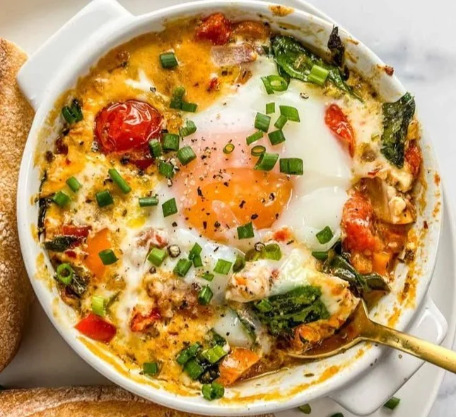 Baked feta eggs with tomatoes and spinach in a serving dish
