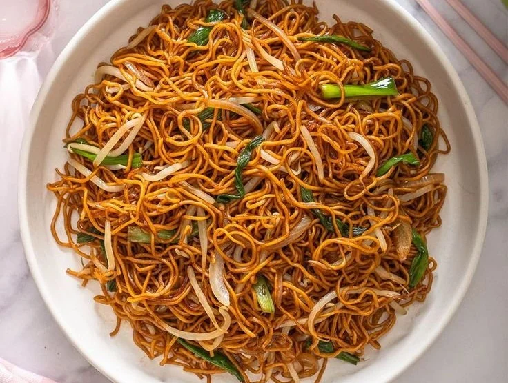 Plate of classic Chinese fried noodles garnished with vegetables and herbs.