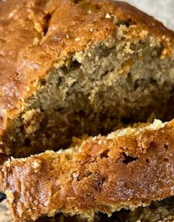 Slice of easy zucchini bread on a cutting board with fresh zucchini beside it
