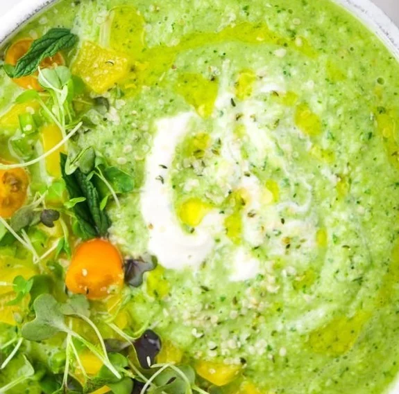 Chilled green gazpacho soup served in a bowl with fresh herbs and vegetables.