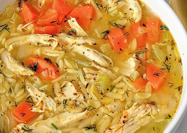 A bowl of Lemon Chicken Orzo Soup garnished with herbs and lemon slices