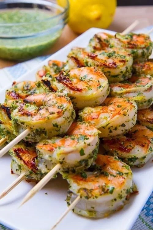 A plate of pesto grilled shrimp garnished with herbs and served with sides.
