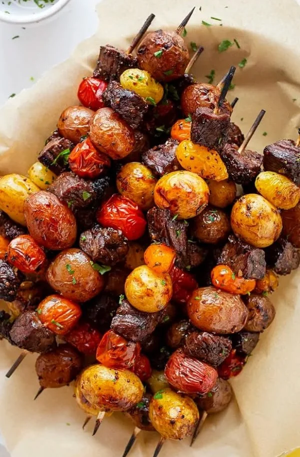 Rosemary garlic steak kebabs on a grill, garnished with fresh herbs.