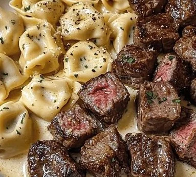 Sizzling Butter Steak Bites served with creamy Alfredo Tortellini on a plate