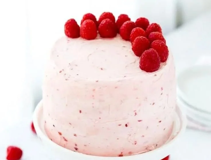 Moist vanilla cake with raspberry filling and frosting topped with fresh berries