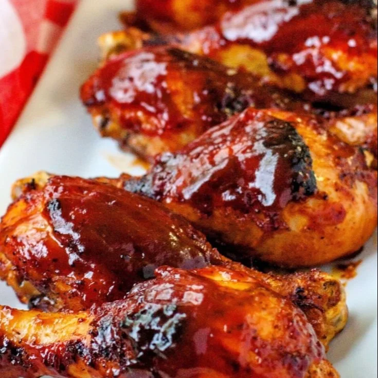 Baked BBQ chicken drumsticks served on a plate with sauce drizzle