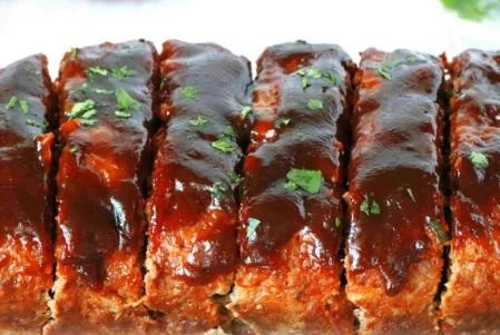 Delicious BBQ meatloaf served on a white plate with BBQ sauce.