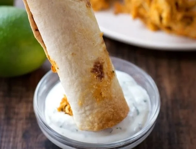 Plate of crispy oven-baked chicken taquitos with garnishes