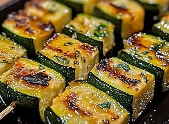 Grilled garlic butter zucchini skewers on a platter with herbs
