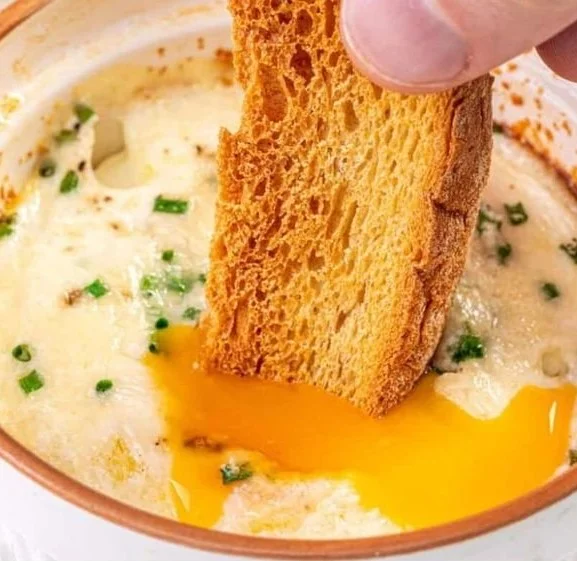Baked shirred eggs topped with herbs and cheese in a ramekin dish.