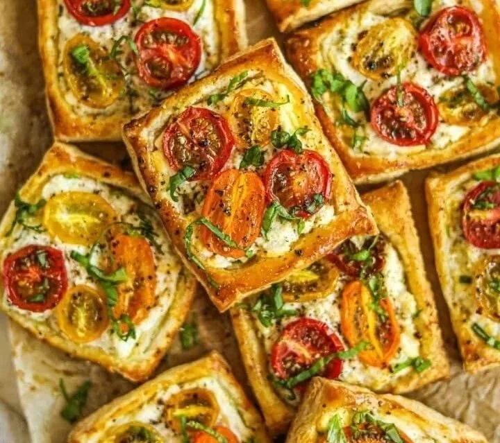 Tomato tartlets with puff pastry topped with fresh herbs and cheese.